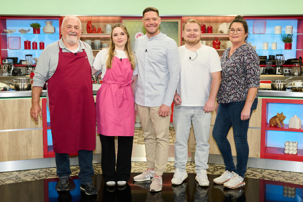 Foto von der ZDF-Sendung "Die Küchenschlacht". Im Vordergrund Moderator und Sternekoch Robin Pietsch, rechts und links neben ihm jeweils zwei Kandidaten. Im Hintergrund ist das Studio des TV-Formats zu erkennen.